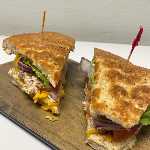 A close-up of a sandwich with layers of lettuce, tomato, cheese, and meat, served on a wooden board.