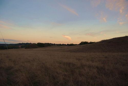 A serene landscape at dusk, featuring rolling hills and a sky with soft clouds and warm hues.