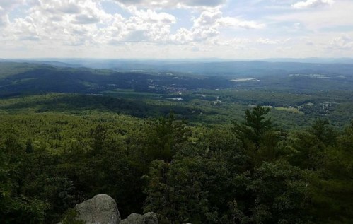 A panoramic view of lush green mountains and valleys under a partly cloudy sky.