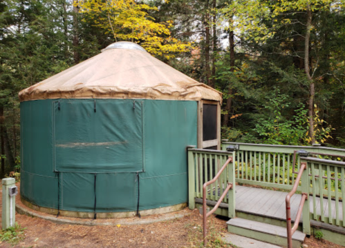 A green yurt surrounded by trees, with a wooden deck leading up to it.