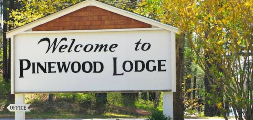 Sign welcoming visitors to Pinewood Lodge, surrounded by trees and greenery.
