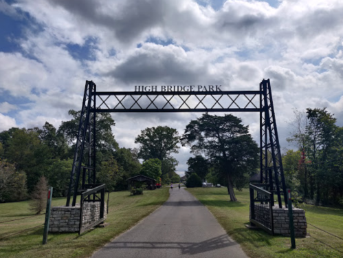 Archway entrance to High Bridge Park, with a pathway leading into the park under a cloudy sky.