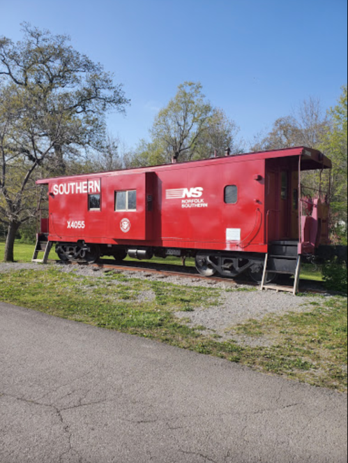 A red caboose labeled "SOUTHERN" parked on a gravel area, surrounded by trees and blue sky.