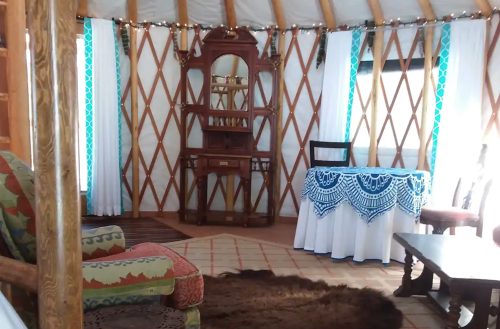 Cozy interior of a yurt featuring a wooden table, chairs, and decorative curtains with a warm, inviting atmosphere.