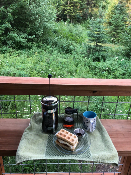 A cozy outdoor breakfast setup with waffles, coffee, and a scenic green backdrop.