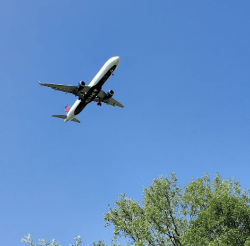 An airplane flying against a clear blue sky, with green trees visible below.