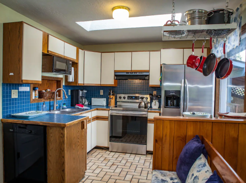 A bright kitchen with wooden cabinets, blue tile backsplash, stainless steel appliances, and a cozy seating area.