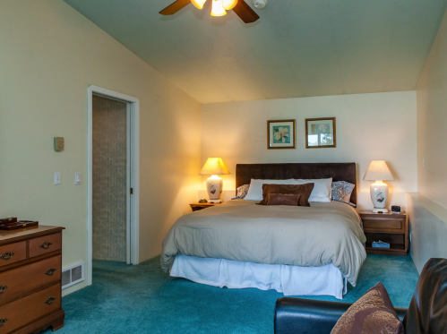 Cozy bedroom with a large bed, nightstands, lamps, and a dresser, featuring soft blue carpet and light-colored walls.