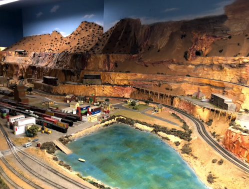 A detailed model train landscape featuring mountains, a lake, and various buildings along the tracks.