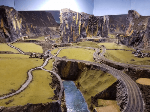 A detailed model landscape featuring mountains, winding roads, and a river, showcasing a miniature train setup.