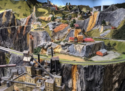 A detailed miniature landscape featuring mountains, buildings, and a winding road, showcasing intricate model scenery.