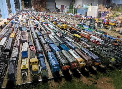 A detailed model train layout featuring numerous colorful train cars and tracks in a realistic setting.