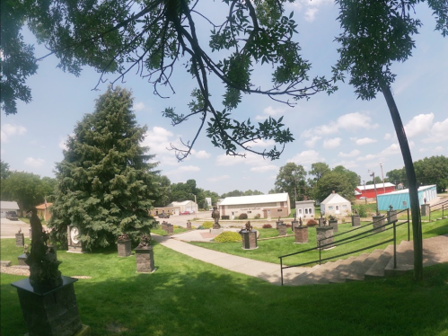 A panoramic view of a cemetery with trees, gravestones, and buildings in the background under a clear blue sky.