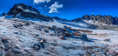 A panoramic view of a snowy landscape featuring the wreckage of an aircraft against a backdrop of mountains.