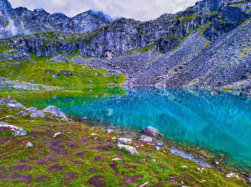 A serene mountain landscape featuring a turquoise lake surrounded by rocky cliffs and lush green grass.