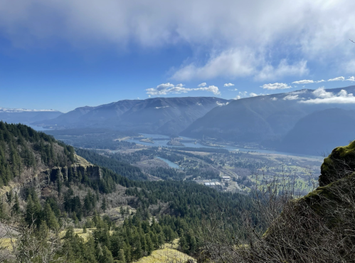 A panoramic view of a valley surrounded by mountains, with lush greenery and a river winding through the landscape.