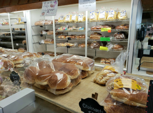 A bakery display with various breads and pastries, including croissants, in clear packaging on shelves.