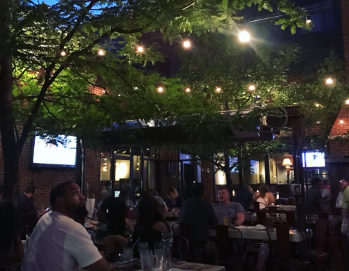 A lively outdoor restaurant scene with string lights, trees, and diners enjoying their meals in a cozy atmosphere.