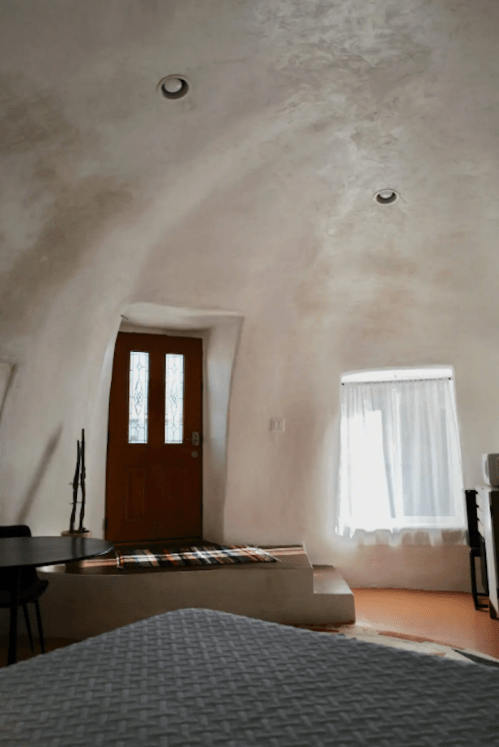 Interior of a unique, curved room featuring a wooden door, a window, and minimalist decor.