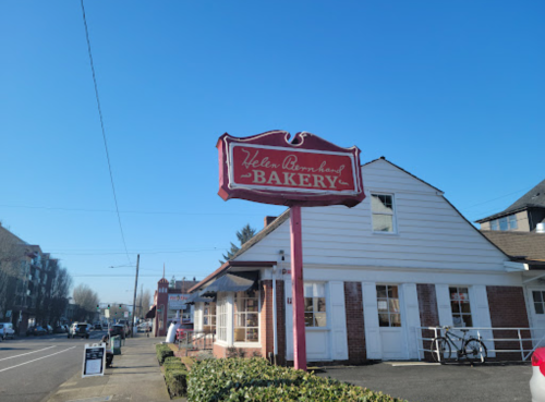 A red sign reading "Helen Bornhold Bakery" outside a white building on a clear day.