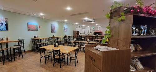 Cozy restaurant interior with wooden tables, chairs, and colorful artwork on the walls, featuring a pizza oven in the background.