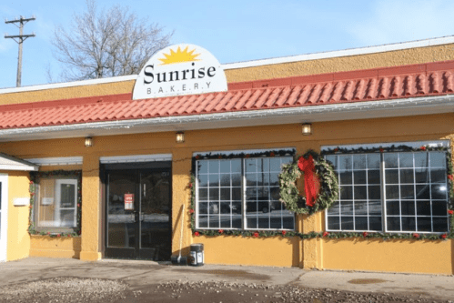 Exterior of Sunrise Bakery, decorated for the holidays with wreaths and garlands, featuring a bright yellow facade.