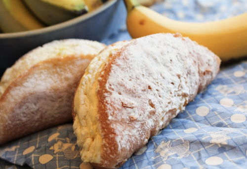 Two powdered sugar-dusted pastries on a blue patterned cloth, with bananas in the background.