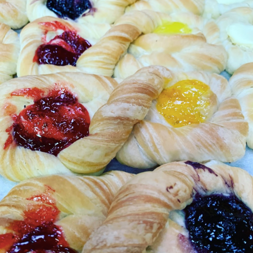 A variety of flaky pastries filled with colorful fruit jams, including red, yellow, and purple fillings.