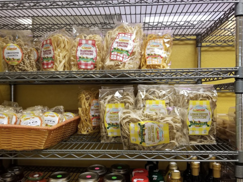 Shelves filled with various packages of pasta, including traditional fettuccine and linguine, in a grocery store.