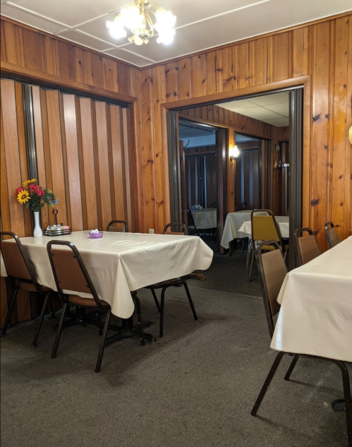 A cozy dining area with wooden walls, tables covered in white cloths, and a flower vase on a table.