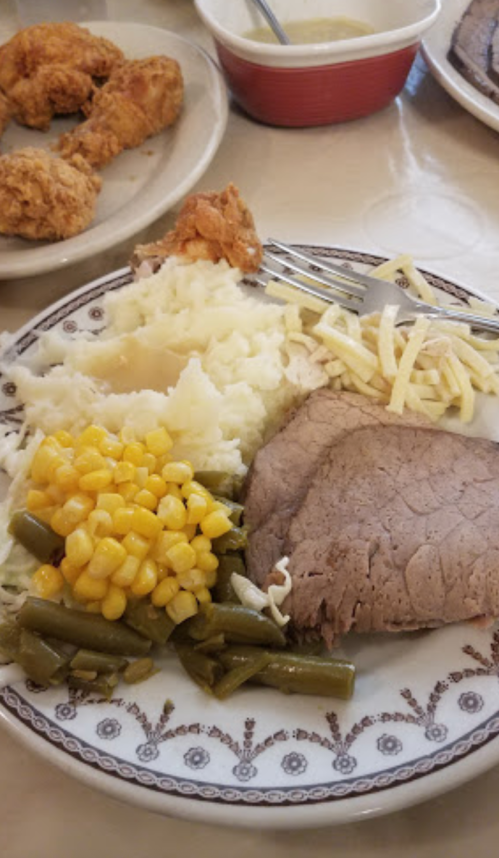 A plate of food featuring sliced roast beef, mashed potatoes, green beans, corn, and fried chicken.