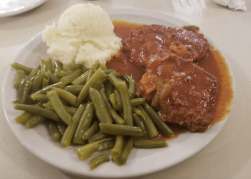 A plate of meatloaf with brown gravy, served with mashed potatoes and green beans.
