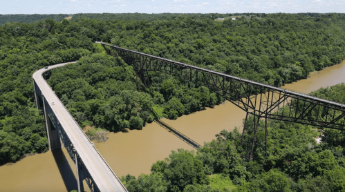 Aerial view of a highway bridge and a railway bridge over a river, surrounded by lush green trees.