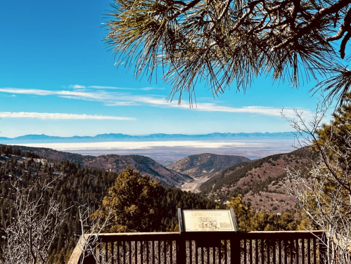 Scenic mountain view with a clear blue sky, overlooking valleys and distant peaks from a viewpoint.