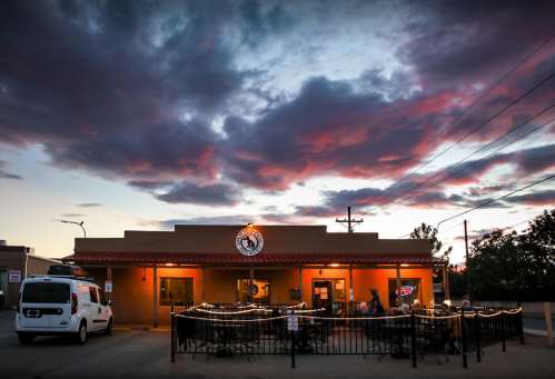 A restaurant exterior at dusk, with colorful clouds and outdoor seating illuminated by warm lights.