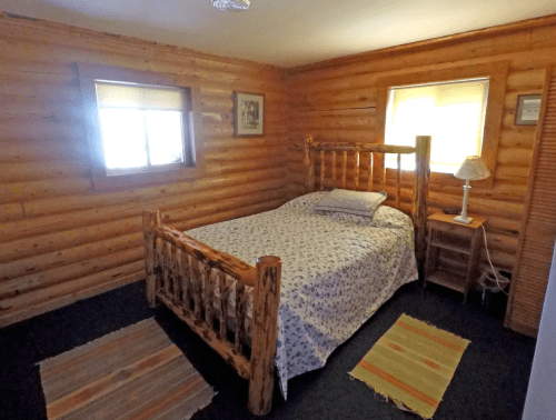 Cozy log cabin bedroom with a wooden bed, patterned bedding, a nightstand, and rustic decor.