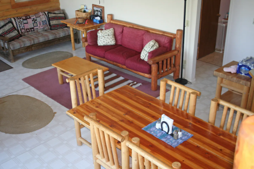 Cozy living area with wooden furniture, a red couch, and a dining table, featuring rugs and a warm, inviting atmosphere.