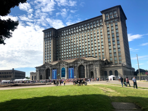 Historic building with a large crowd in front, green grass in the foreground, and a clear blue sky above.