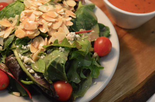 A fresh salad with mixed greens, cherry tomatoes, sliced almonds, and a small bowl of dressing on the side.