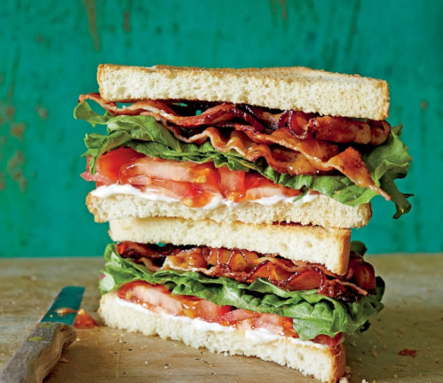 A stacked sandwich with layers of bacon, lettuce, tomato, and mayonnaise between slices of white bread.