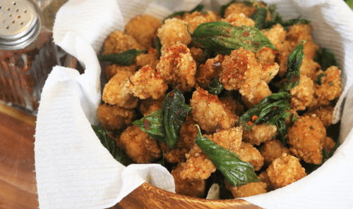 A wooden bowl filled with crispy fried bites, garnished with fresh green basil leaves.