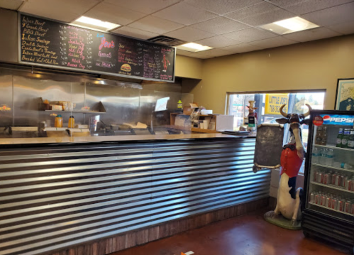 A casual eatery interior featuring a menu board, grill area, and a soda fridge with a cartoon cow mascot.