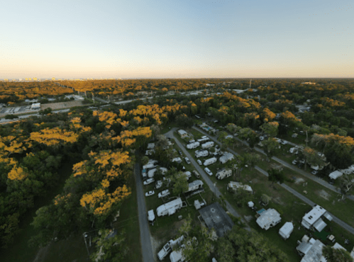 Aerial view of a campground surrounded by trees, with RVs and a clear sky in the background.