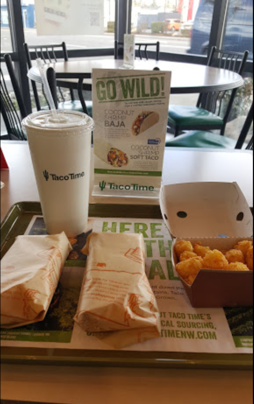 A TacoTime meal featuring two wrapped tacos, a box of crispy bites, and a drink on a tray in a casual dining setting.