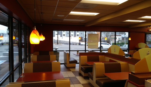 Interior of a fast-food restaurant with empty booths, large windows, and pendant lighting.