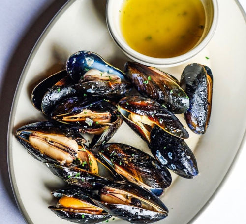 A plate of steamed mussels served with a small bowl of dipping sauce.