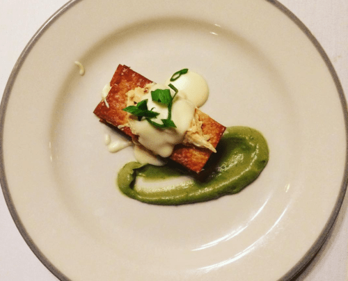 A plated dish featuring a rectangular piece of crispy food topped with sauce and garnished with green onions, beside a green puree.