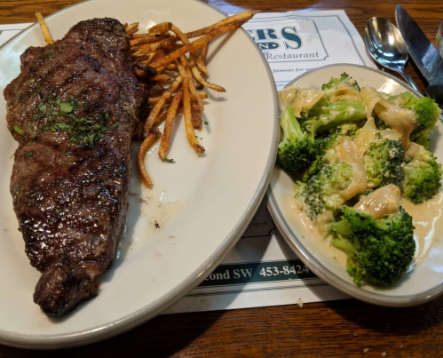 A plate featuring a grilled steak with fries and a side of broccoli in a creamy sauce.
