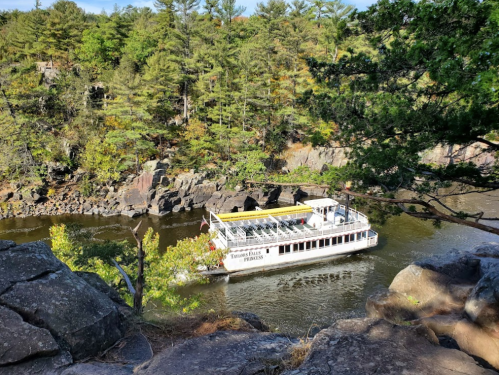 A scenic view of a boat navigating a river surrounded by lush greenery and rocky cliffs.