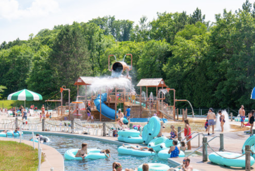 A vibrant water park scene with a large slide, splash features, and people enjoying the pool and lazy river.